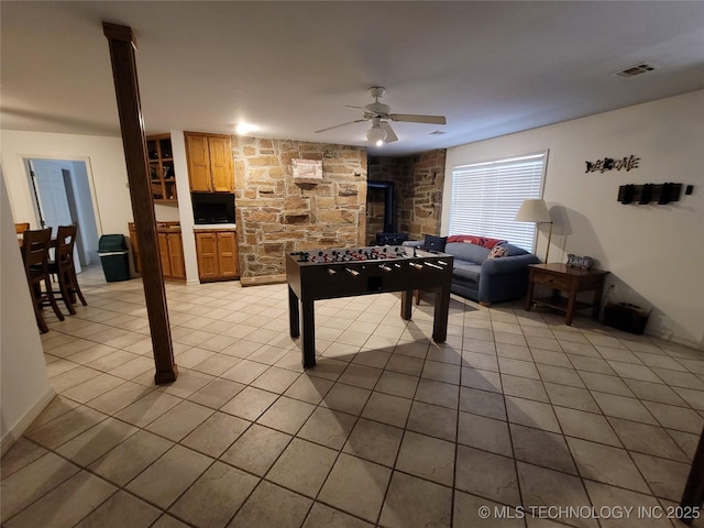 rec room with a wood stove, light tile patterned floors, and ceiling fan