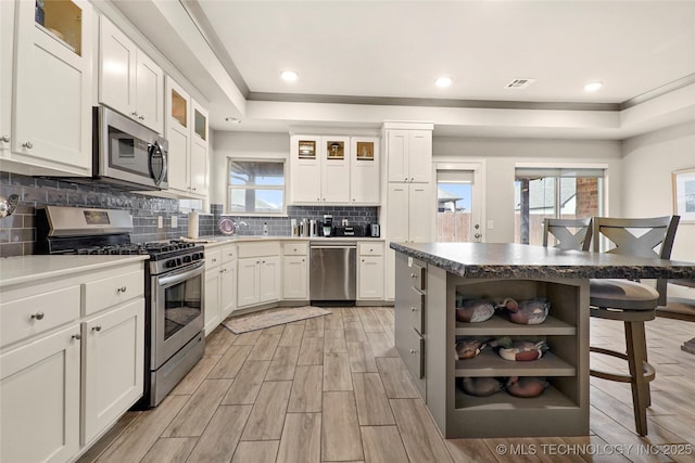 kitchen with tasteful backsplash, appliances with stainless steel finishes, a raised ceiling, and white cabinets