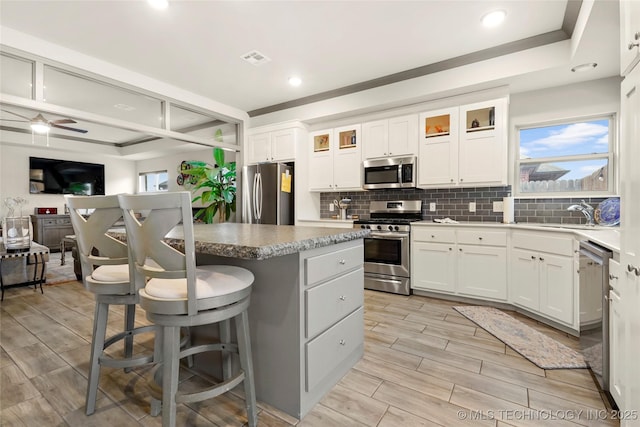 kitchen featuring a kitchen breakfast bar, stainless steel appliances, a center island, white cabinets, and decorative backsplash