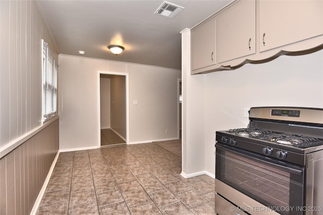 kitchen featuring stainless steel range with gas cooktop, light tile patterned floors, and wooden walls