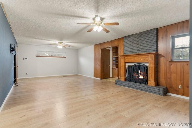 unfurnished living room with light hardwood / wood-style flooring, a fireplace, a textured ceiling, and wood walls