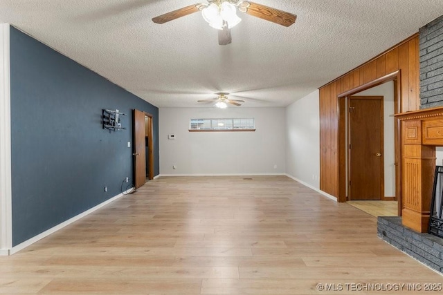 interior space featuring wood walls, a textured ceiling, ceiling fan, a fireplace, and light hardwood / wood-style floors