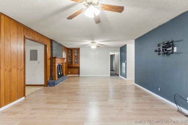 unfurnished living room featuring a brick fireplace, light hardwood / wood-style flooring, wooden walls, and a textured ceiling