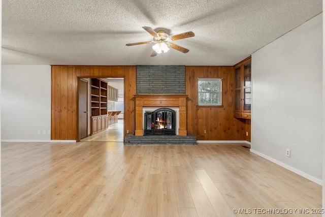 unfurnished living room with ceiling fan, wooden walls, light hardwood / wood-style floors, a textured ceiling, and a brick fireplace