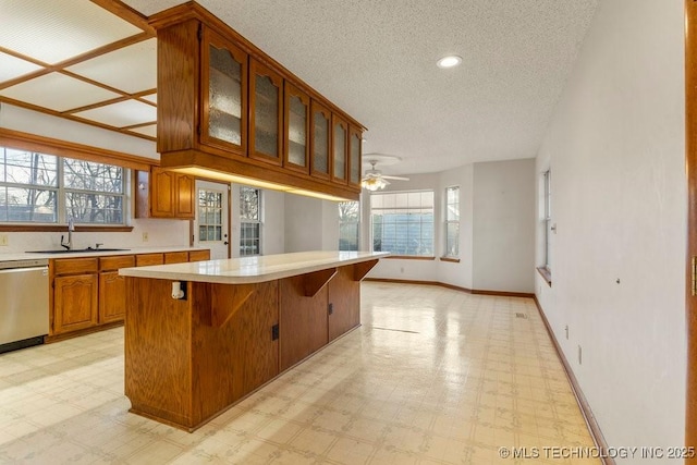 kitchen featuring sink, a center island, a textured ceiling, stainless steel dishwasher, and ceiling fan