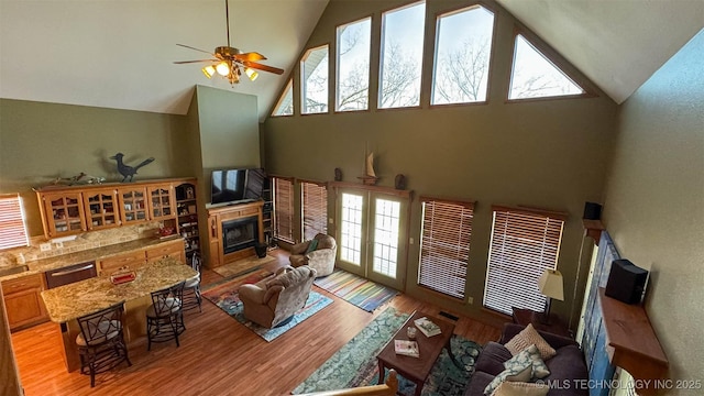 living room featuring ceiling fan, high vaulted ceiling, and light hardwood / wood-style flooring