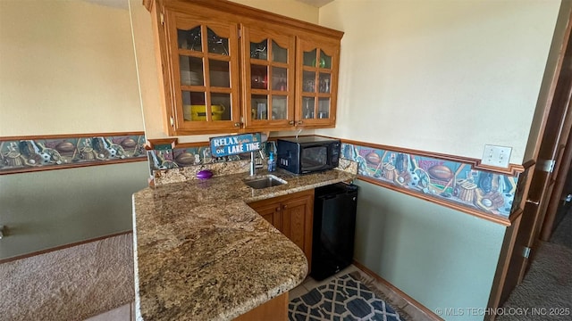 kitchen featuring light stone countertops, sink, kitchen peninsula, and black appliances