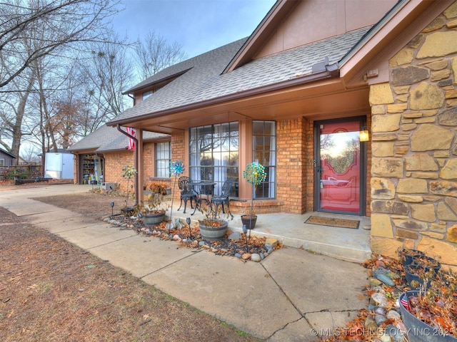 view of exterior entry with stone siding, a shingled roof, brick siding, and stucco siding