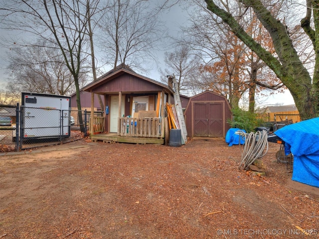 view of front of home with a storage shed, a gate, fence, and an outbuilding