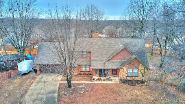 view of front facade with stone siding, a chimney, concrete driveway, and roof with shingles