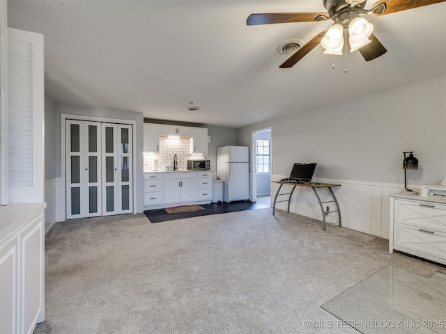 interior space featuring light carpet, visible vents, a ceiling fan, wainscoting, and a sink