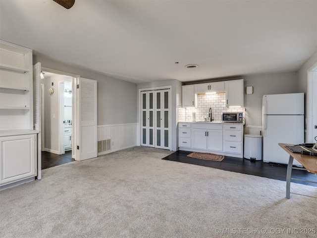 unfurnished living room with dark colored carpet, a wainscoted wall, visible vents, and a sink