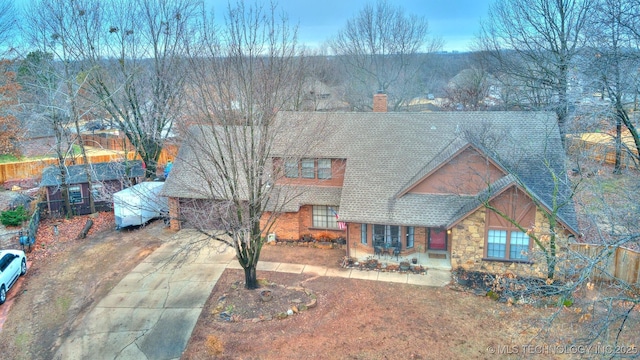 view of front of home with stone siding, a shingled roof, a chimney, and a patio