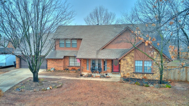 view of front facade with stone siding, concrete driveway, a shingled roof, and fence