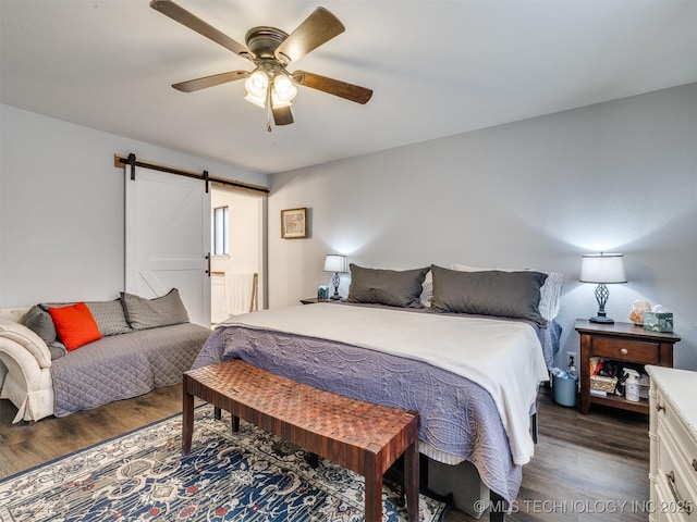 bedroom with ceiling fan, a barn door, and dark hardwood / wood-style flooring