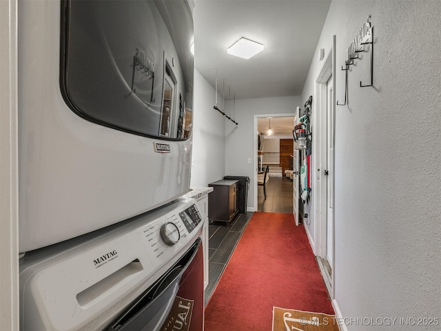 clothes washing area with a textured wall, laundry area, stacked washer and clothes dryer, and baseboards