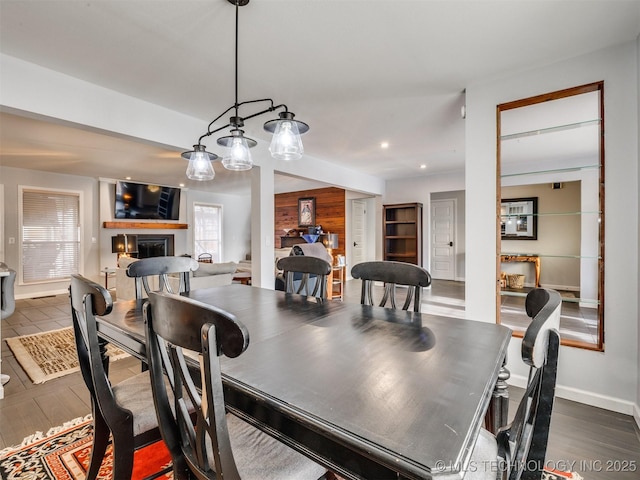 dining space with wooden walls, baseboards, a glass covered fireplace, dark wood-type flooring, and recessed lighting