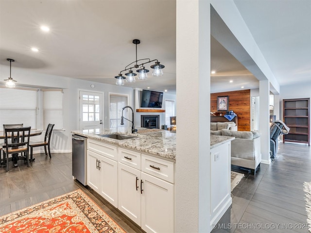 kitchen with decorative light fixtures, dishwasher, sink, white cabinets, and light stone counters