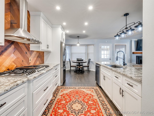 kitchen with pendant lighting, stainless steel appliances, white cabinetry, a sink, and wall chimney exhaust hood