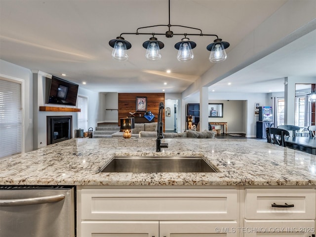 kitchen featuring light stone counters, open floor plan, a fireplace, white cabinetry, and a sink