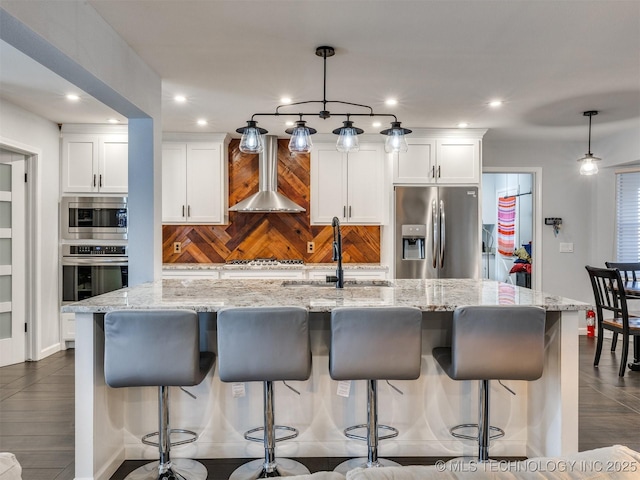 kitchen featuring white cabinets, appliances with stainless steel finishes, a large island, and wall chimney range hood