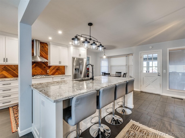 kitchen featuring white cabinets, wall chimney range hood, appliances with stainless steel finishes, a kitchen bar, and pendant lighting