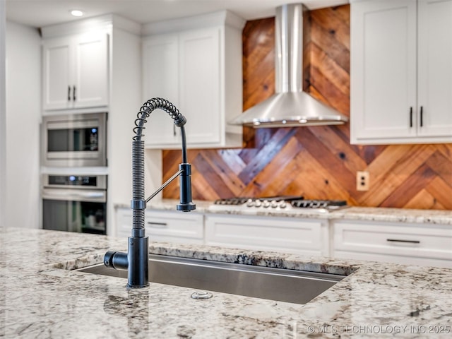 kitchen featuring white cabinetry, stainless steel appliances, and wall chimney range hood