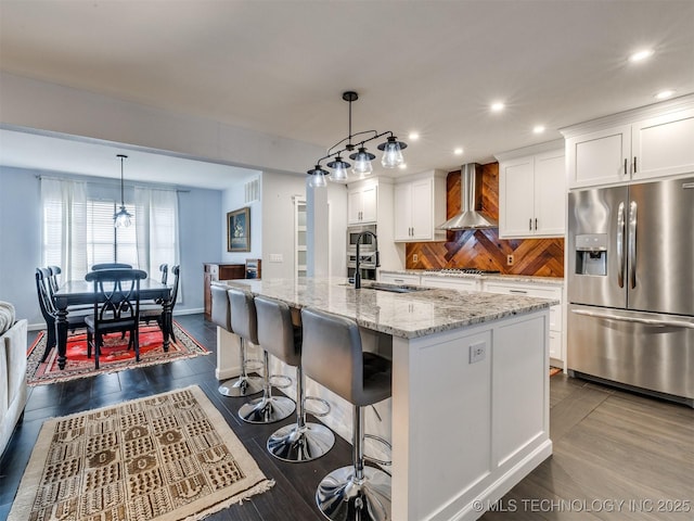 kitchen featuring white cabinetry, wall chimney range hood, stainless steel appliances, and a center island with sink