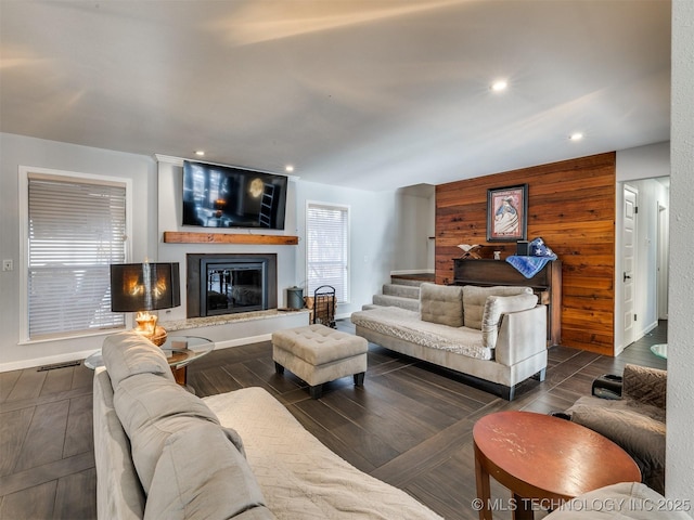 living area featuring wooden walls, visible vents, a glass covered fireplace, stairs, and recessed lighting