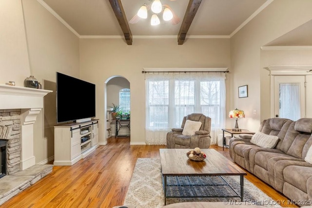 living room featuring beam ceiling, crown molding, a stone fireplace, and light hardwood / wood-style floors