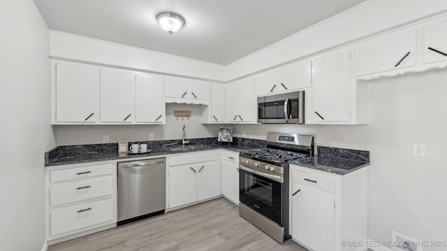 kitchen featuring sink, appliances with stainless steel finishes, dark stone countertops, light hardwood / wood-style floors, and white cabinets