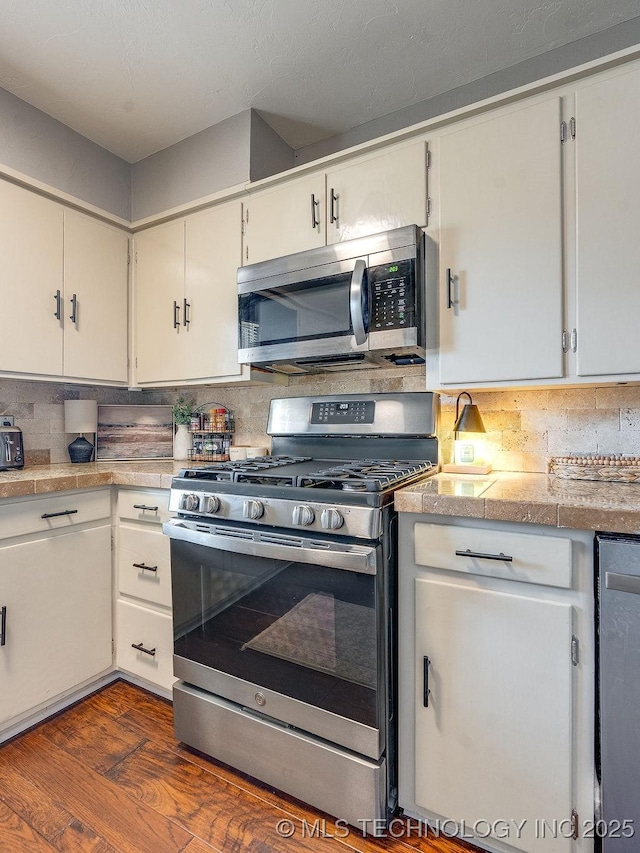 kitchen featuring stainless steel appliances, white cabinetry, dark wood-type flooring, and backsplash