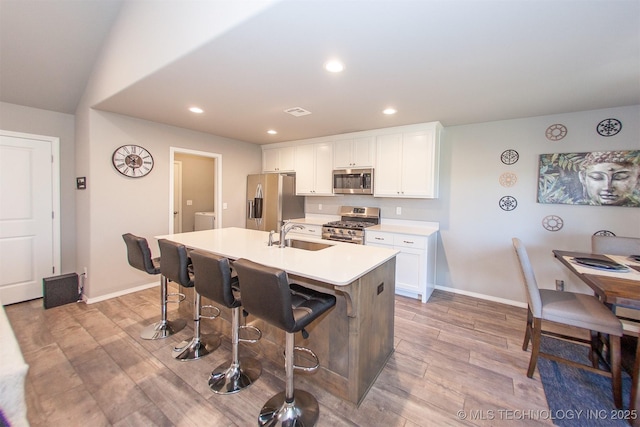 kitchen with white cabinetry, sink, a kitchen breakfast bar, stainless steel appliances, and a center island with sink