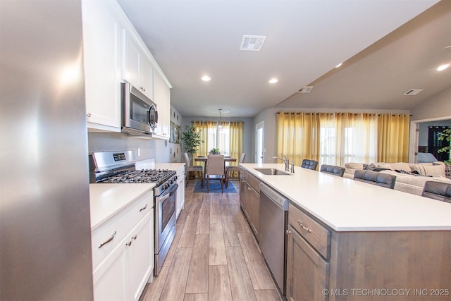 kitchen with sink, white cabinets, a kitchen island with sink, stainless steel appliances, and light hardwood / wood-style flooring