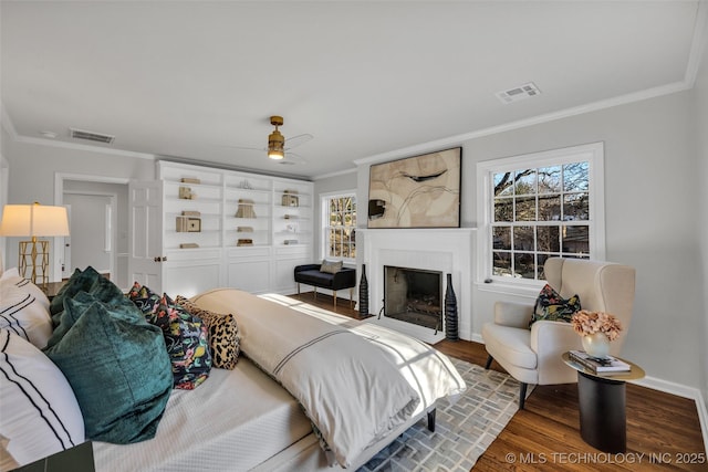 bedroom with a fireplace with flush hearth, visible vents, wood finished floors, and ornamental molding