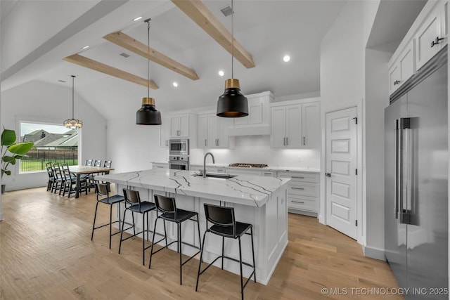 kitchen featuring built in appliances, white cabinetry, a kitchen island with sink, and decorative light fixtures