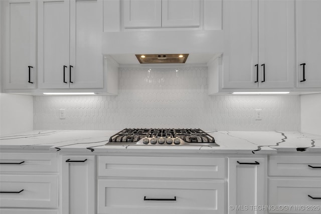 kitchen with premium range hood, stainless steel gas cooktop, white cabinetry, light stone counters, and decorative backsplash