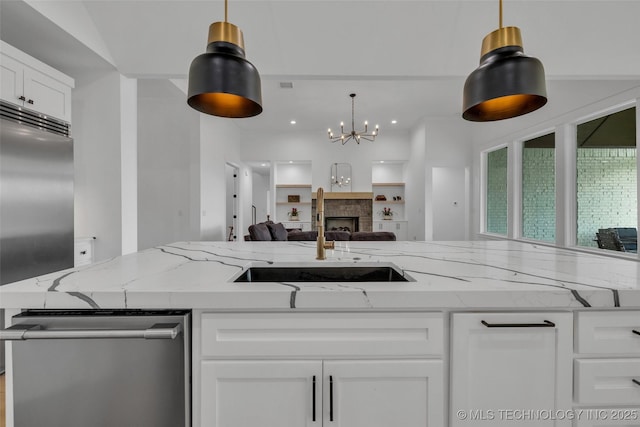 kitchen featuring decorative light fixtures, sink, white cabinets, light stone counters, and stainless steel appliances