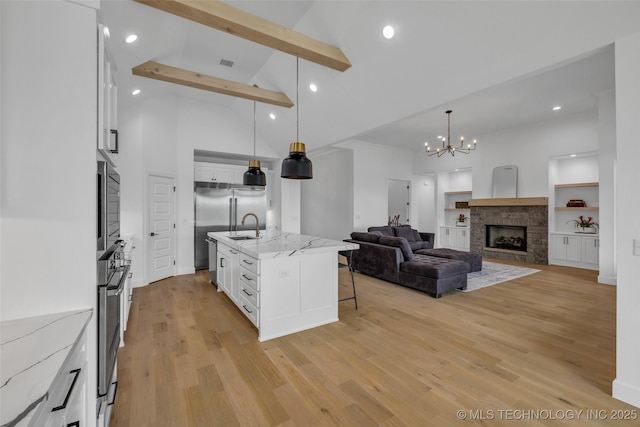 kitchen with decorative light fixtures, beam ceiling, light stone countertops, a kitchen island with sink, and white cabinets