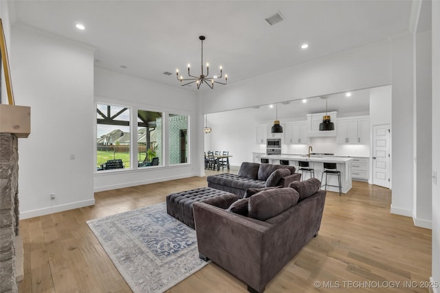 living room with sink, ornamental molding, a chandelier, and light wood-type flooring