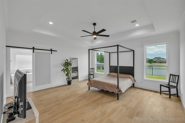 bedroom featuring a barn door, ceiling fan, a tray ceiling, and light hardwood / wood-style flooring