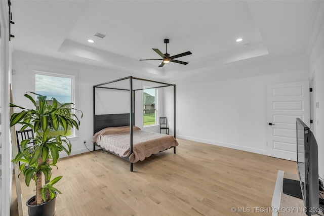 bedroom featuring a tray ceiling, ceiling fan, and light wood-type flooring