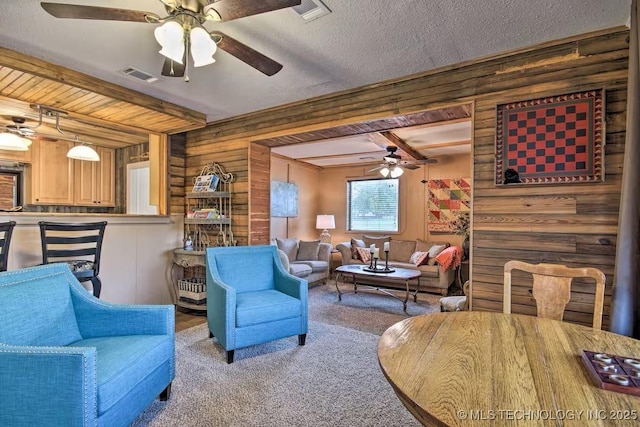 living room featuring wood walls, carpet, ceiling fan, a textured ceiling, and beam ceiling