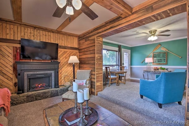 carpeted living room with crown molding, ceiling fan, a stone fireplace, and wood walls