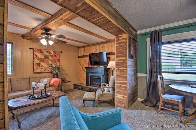 carpeted living room with ceiling fan, beam ceiling, a textured ceiling, and wood walls