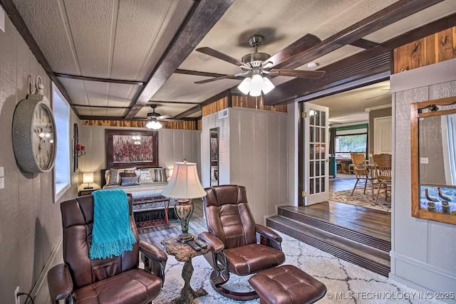 living room with beamed ceiling, ceiling fan, and wood walls