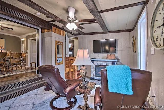 living room with crown molding, ceiling fan, hardwood / wood-style floors, beam ceiling, and a stone fireplace