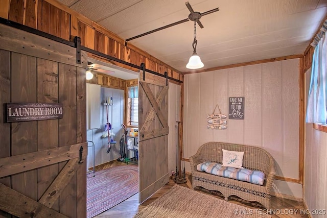 mudroom with ceiling fan, wooden walls, wood-type flooring, and a barn door