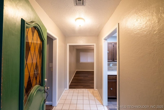 hall with a textured ceiling and light tile patterned floors