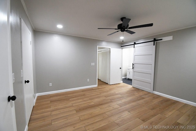 unfurnished bedroom featuring crown molding, ensuite bath, a barn door, and light hardwood / wood-style floors